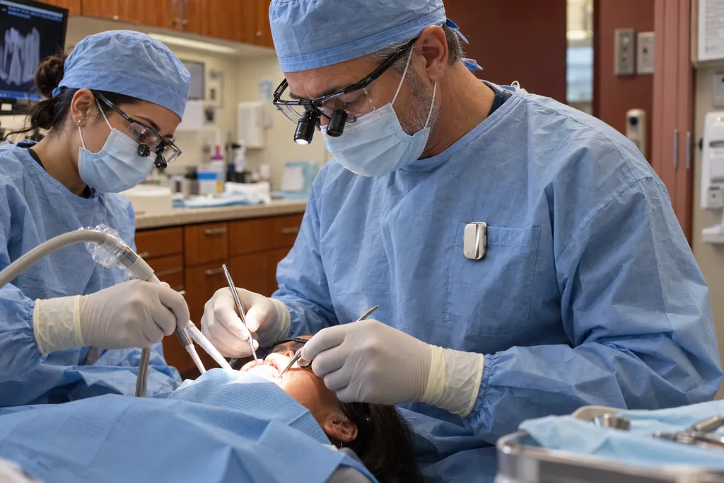 Illustration: a dentist in loupes, with the Vault capsule clipped to his gown pocket, treats a patient beside an assistant.