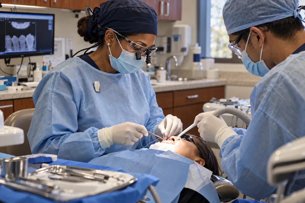 Illustration: a dentist in loupes, with the Vault capsule clipped to her gown, places a suture while an assistant helps.